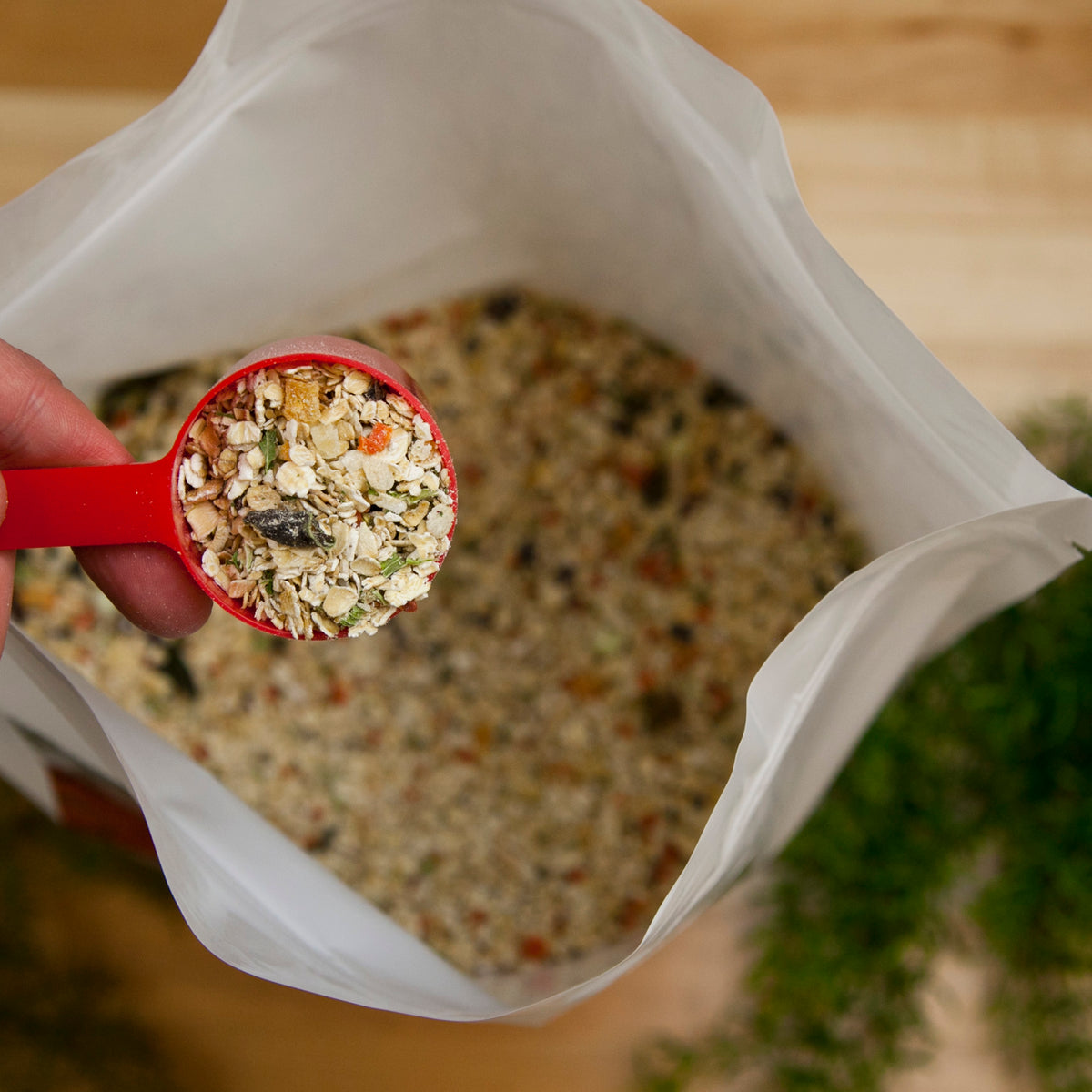 Red measuring scoop filled with mixed grain and herb blend held over open resealable bag of the same mixture