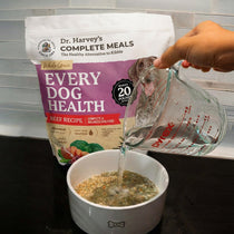 Dr. Harvey's Every Dog Health Beef Recipe dog food bag with water being poured from Pyrex measuring cup into dog bowl